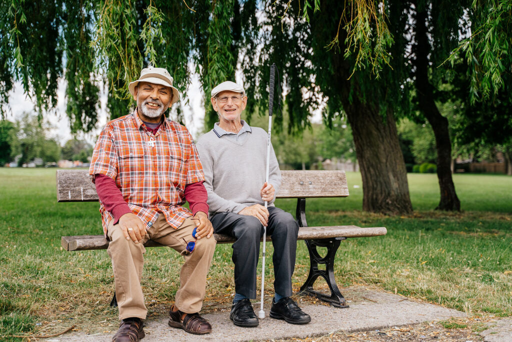 Parry, an MAB client and an MAB Volunteer named David. 
Sitting on a park bench both smiling looking at the camera